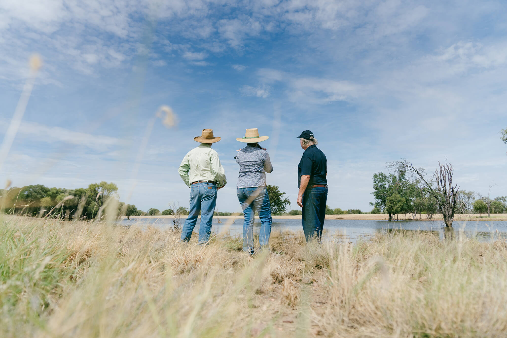 Three people on farm looking at a dam